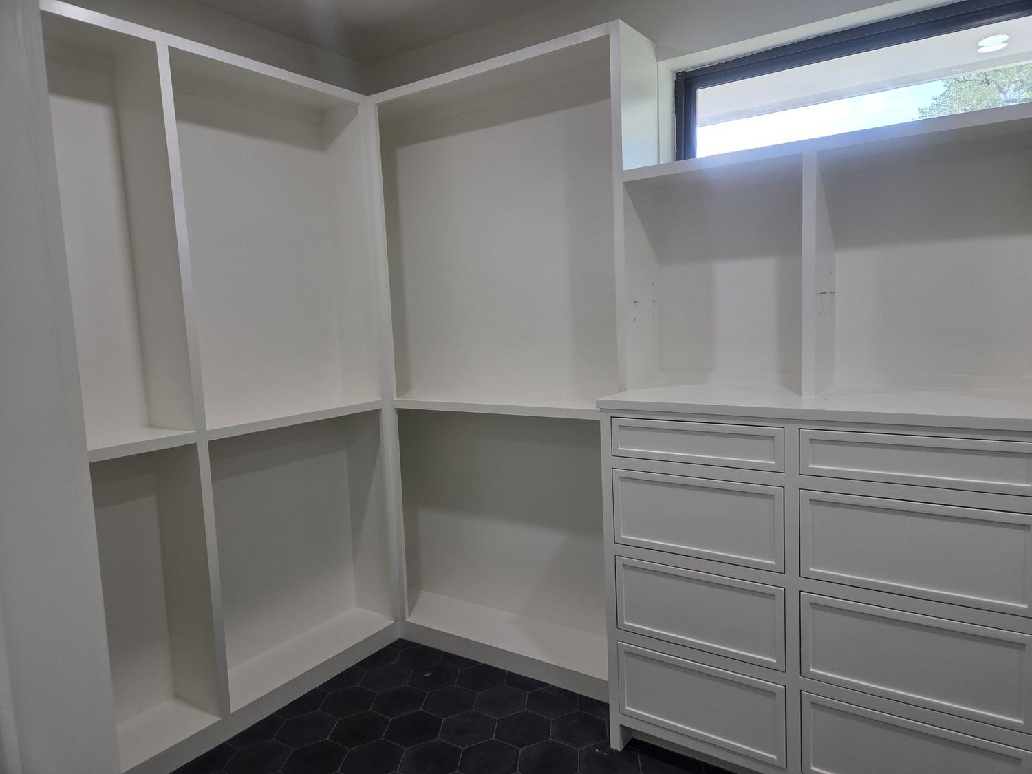 Custom walk-in closet with built-in shelving, drawers, and dark hexagonal tile flooring
