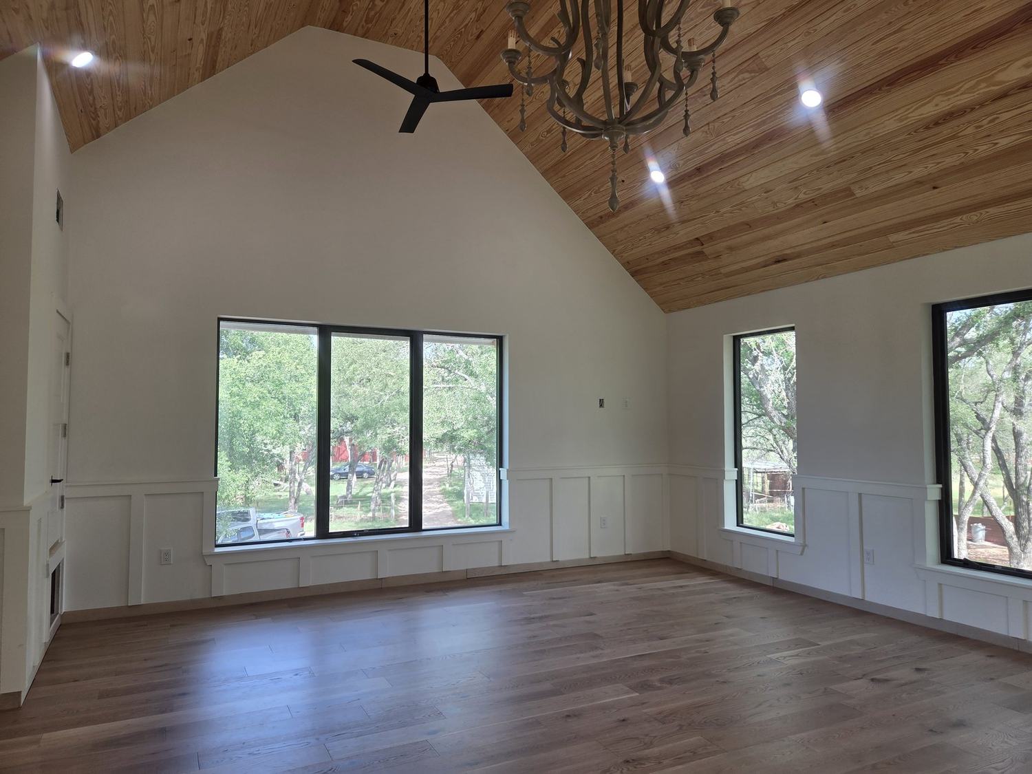 Finished custom home living room with vaulted wood ceiling, large windows, wainscoting, and wood flooring