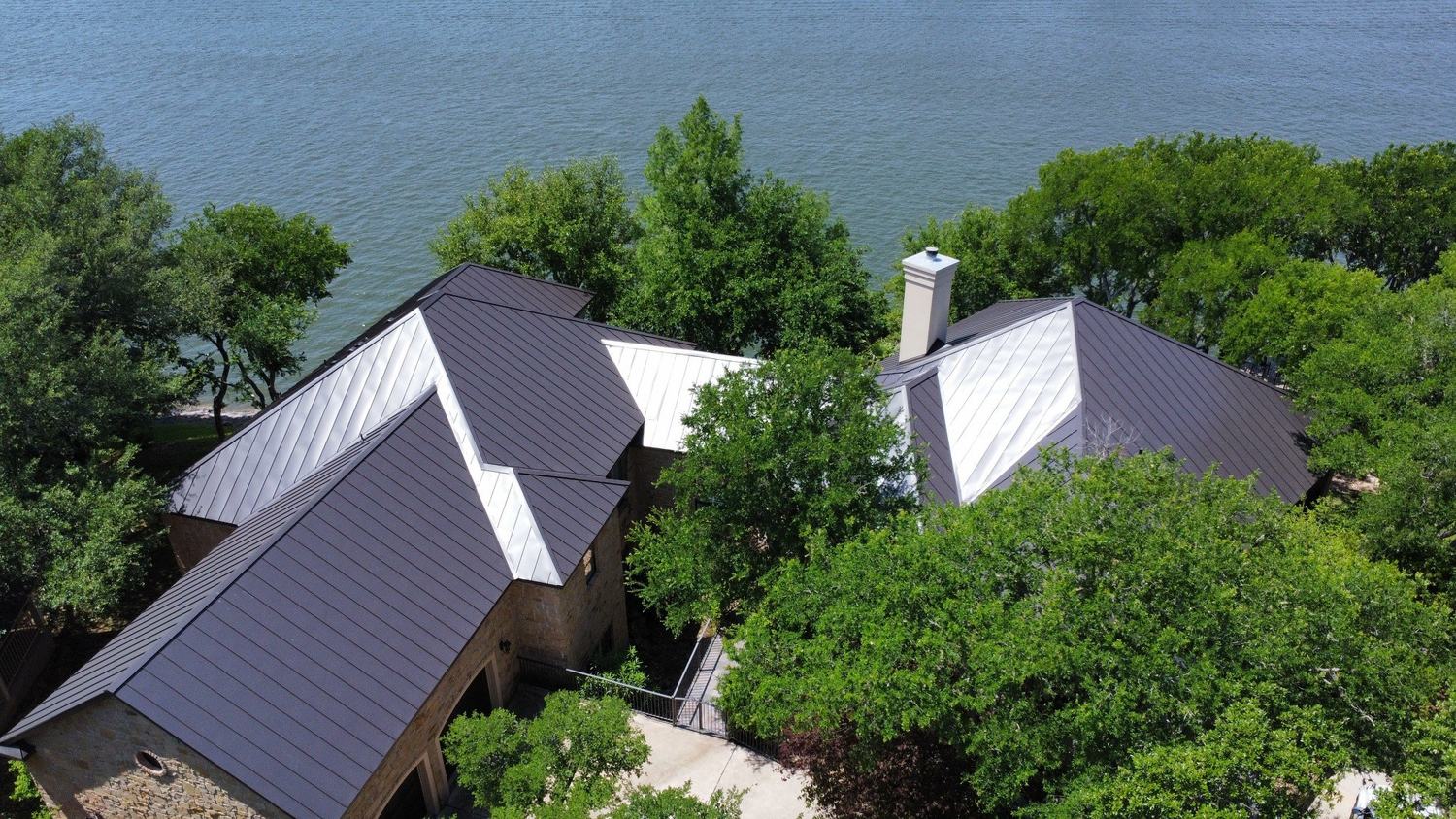 Aerial view of a lakeside home with dark and light standing-seam metal roof sections
